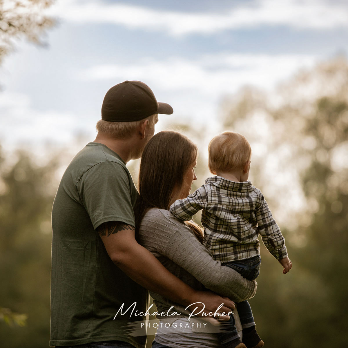 Familie steht eng umschlungen im Freien und blickt gemeinsam in die weiche Abendsonne.